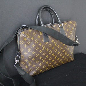 May include: Brown and tan monogrammed briefcase with black handles and a detachable shoulder strap. The bag features a zipper closure and silver-tone hardware. The bag is made of a durable material and is suitable for carrying documents and other essentials.