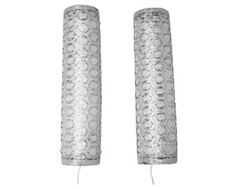 May include: Two cylindrical silver and white decorative lamps. The lamps have a honeycomb pattern and a wire extending from the bottom. The lamps are illuminated from within.