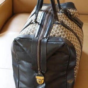 Puede incluir: Una bolsa de viaje de cuero marr&oacute;n y negro con un patr&oacute;n tejido. La bolsa tiene una cremallera y una cerradura dorada.