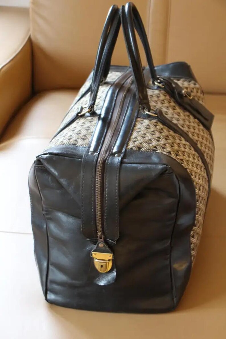 Puede incluir: Una bolsa de viaje de cuero marr&oacute;n y negro con un patr&oacute;n tejido. La bolsa tiene una cremallera y una cerradura dorada.