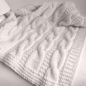 May include: White knitted blanket with a cable knit pattern.