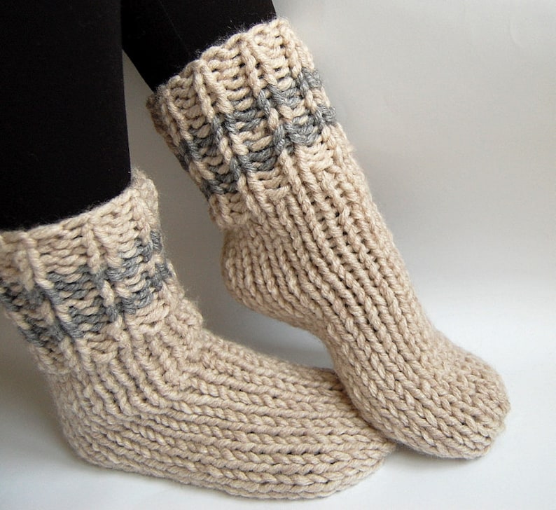 May include: A pair of beige knitted socks with gray stripes around the cuff. The socks are thick and cozy, perfect for cold weather.