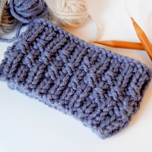 May include: A close-up of a gray knitted fabric with a textured pattern. Two wooden knitting needles are lying on a white surface.