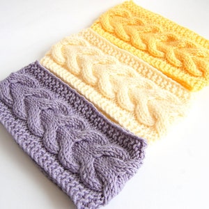 May include: Three knitted headbands in a gradient of purple, cream, and yellow. Each headband features a cable knit pattern.
