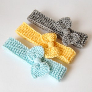 May include: Three knitted headbands with bows in different colours: light blue, yellow and grey.