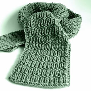 May include: A sage green knitted scarf with a textured pattern. The scarf is folded and draped, showcasing the intricate stitch work. The soft, muted colour and detailed texture create a cosy, handmade aesthetic.