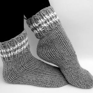 May include: A pair of grey knitted socks with white stripes around the top of the socks.