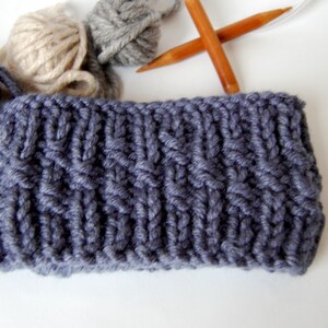 May include: A close-up of a gray knitted headband with a cable knit pattern. The headband is made with thick yarn and has a simple, classic design.