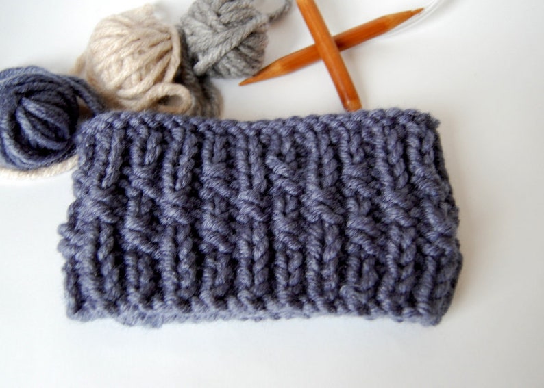 May include: A close-up of a gray knitted headband with a cable knit pattern. The headband is made with thick yarn and has a simple, classic design.