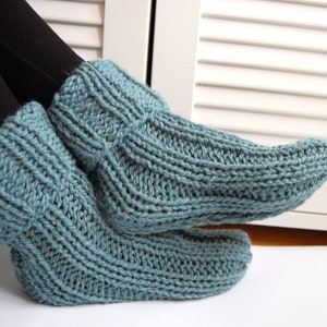 Könnte beinhalten: Ein Paar tealblaue gestrickte Hausschuhe. Die Socken sind aus dickem Garn gefertigt und haben eine gerippte Struktur.