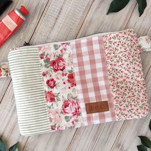 May include: A patchwork cosmetic bag with a floral, striped, and gingham pattern. The bag features a handle and a zip closure. The colour palette includes pink, white, and green. The label reads "EBONY RED".