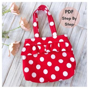 Pode incluir: Uma bolsa de tecido vermelha com padrão de bolinhas brancas e um babado horizontal na frente. A bolsa tem duas alças combinando com bolinhas vermelhas e brancas. Um gráfico circular na imagem contém o texto PDF Step By Step.