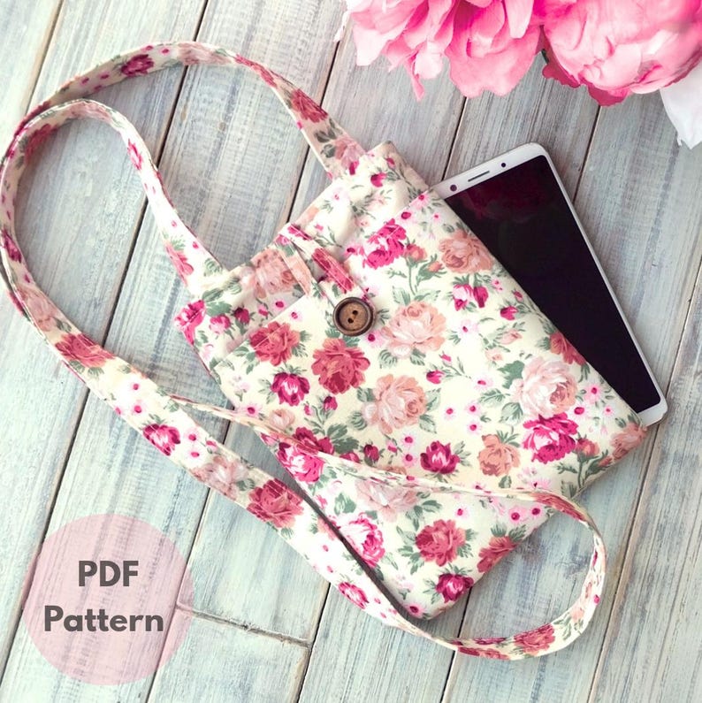 May include: A floral print tote bag with a long strap and a wooden button closure. The bag features a cream background with pink and red roses. The words "PDF Pattern" are visible in the lower left corner.