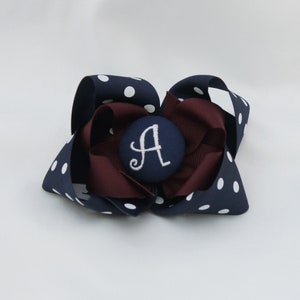 May include: A navy blue and white polka dot hair bow with a maroon center and a navy blue button with the letter "A" embroidered in white.