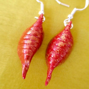 May include: A pair of red and gold earrings shaped like seashells with silver hooks.