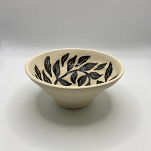 May include: A white ceramic bowl with a black floral design. The bowl is slightly angled and the design is visible on the inside of the bowl.