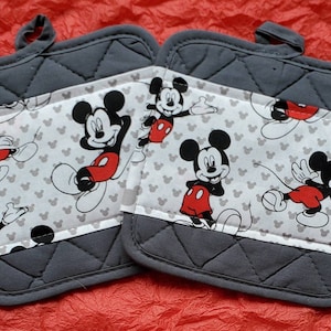 Może przedstawiać: Dwa szare, pikowane uchwyty do garnków z białym panelem z tkaniny, na którym znajduje się powtarzający się wzór głów Myszki Miki. Panel z tkaniny ma szary obramowanie.