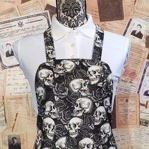 Peut inclure: Un tablier noir et blanc avec un motif de crânes et de roses. Le tablier a des bretelles réglables et une grande poche sur le devant.