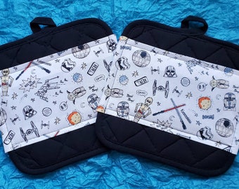 Könnte beinhalten: Ein Set aus zwei schwarzen, gesteppten Topflappen mit weißen Stoffbahnen, die ein Star Wars-Motiv zeigen. Das Muster enthält Figuren wie Darth Vader, R2-D2, C-3PO und den Millennium Falcon.
