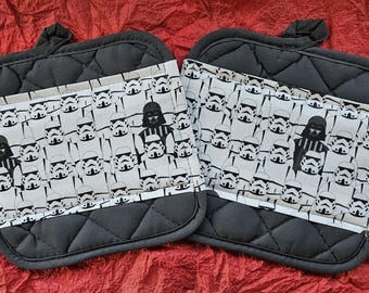 Könnte beinhalten: Ein Paar schwarze, gesteppte Ofenhandschuhe mit einem weißen und schwarzen Muster aus Sturmtruppen und Darth Vader. Die Handschuhe sind aus gestepptem Stoff und haben eine Schlaufe zum Aufhängen.