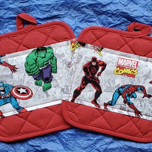 May include: Two red quilted oven mitts with a Marvel Comics theme. The center panel features comic book panels with characters like Spider-Man, Captain America, and the Hulk. The Marvel Comics logo is visible. Each mitt has a loop for hanging.
