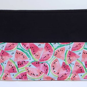 May include: Black fabric apron with a watermelon print. The apron has three pockets and ties at the waist.