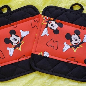 May include: Two black and red quilted pot holders with a Mickey Mouse pattern. The pot holders have a loop for hanging.