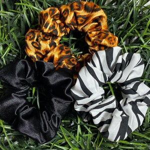 May include: Three hair scrunchies in different patterns. One is black satin, one is black and white zebra print, and one is brown and gold leopard print.