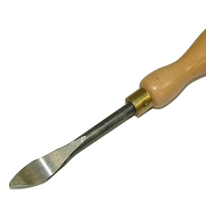 Puede incluir: Un formón para trabajar la madera con un mango de madera de color marrón claro y una hoja de metal plateado. La herramienta está diseñada para dar forma y tallar madera. El formón está en ángulo y tiene una hoja curva. El mango está unido a la hoja con una férula de latón.