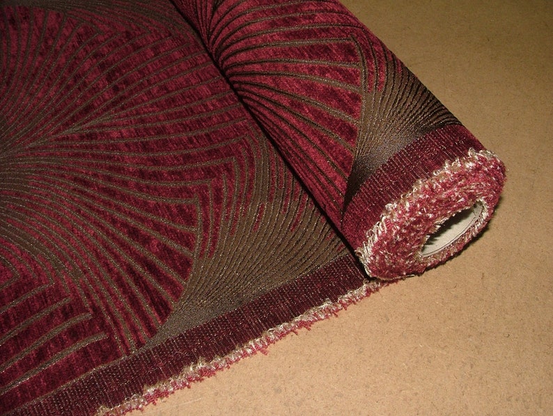 May include: A roll of burgundy fabric with a brown geometric pattern. The fabric has a textured surface and a fringed edge.