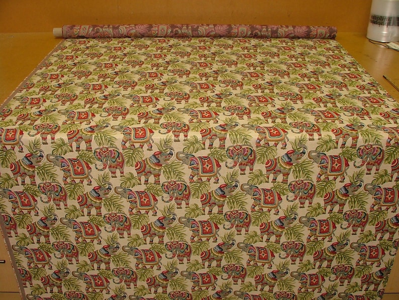 May include: A beige fabric with a repeating pattern of colorful elephants and green leaves. The elephants are decorated with red, blue, and gold accents.