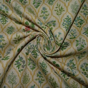 May include: Close-up of a beige fabric with a repeating floral pattern. The design features green, blue, and pink floral elements within a gold trellis-like framework. The fabric is gathered, showing its texture and folds.