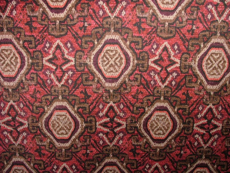 May include: Close-up of a patterned fabric with a repeating geometric design. The pattern features a mix of red, brown, and cream colors. The design includes diamond and oval shapes, creating a textured appearance.
