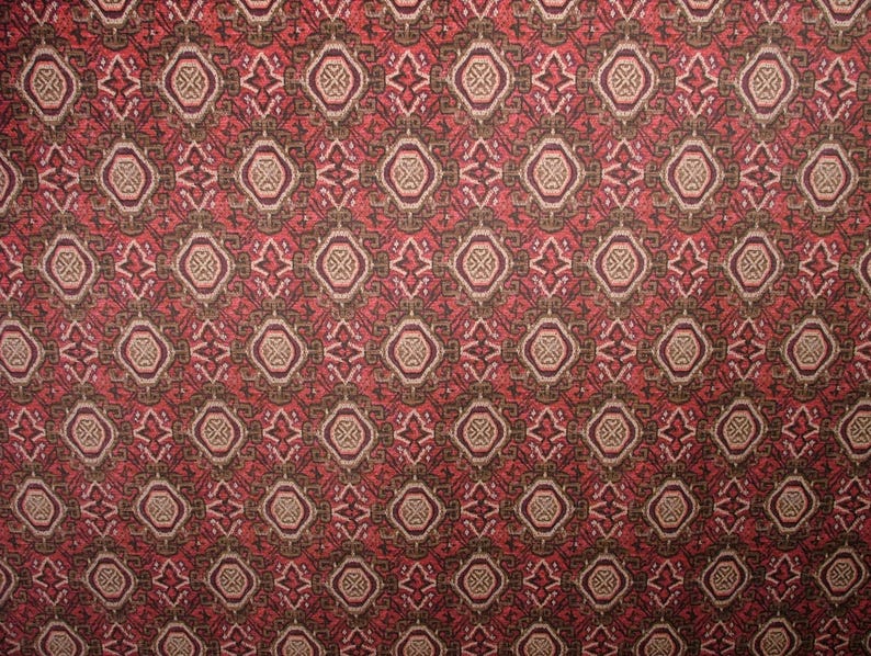May include: Close-up of a patterned fabric with a repeating geometric design. The pattern features diamond and circular shapes in shades of red, brown, and beige. The fabric has a textured appearance, suggesting a woven material.