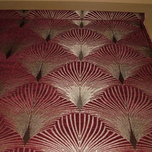 May include: Red fabric with a gold and brown geometric pattern of overlapping fan shapes.