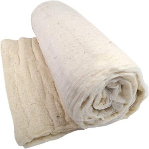 May include: A roll of white cotton wadding, a natural fibre used for stuffing and padding. The wadding is rolled up and ready to be used for various crafting and sewing projects.