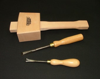 May include: A light-colored wooden mallet with the text Draper Expert printed on the head, accompanied by two hand tools featuring light wooden handles, metal shafts, and brass ferrules, including a flat chisel and a V-shaped gouge.