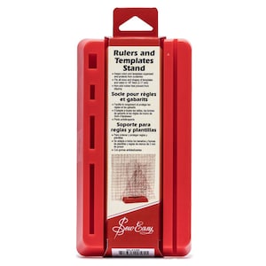 Peut inclure: Support rouge en plastique pour règles et gabarits avec des fentes pour maintenir les règles et les gabarits. Le support a une base en caoutchouc antidérapante. Le texte sur le support indique "Rulers and Templates Stand", "Socle pour règles et gabarits", et "Soporte para reglas y plantillas".