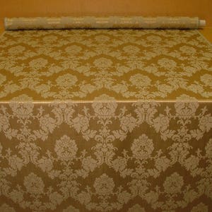 K&ouml;nnte beinhalten: Eine Rolle goldfarbener Stoff mit einem wei&szlig;en Damastmuster. Der Stoff hat einen dezenten Glanz und ein luxuri&ouml;ses Gef&uuml;hl.