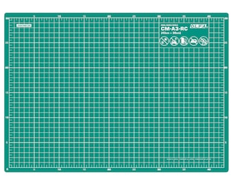 Könnte beinhalten: Eine grüne, selbstheilende Schneidematte mit einem Rastermuster. Die Matte ist 43 cm x 30 cm groß und hat den Text "CM-A3-RC OLFA" aufgedruckt. Die Matte ist in Japan hergestellt.