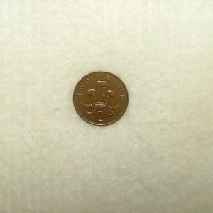 May include: A copper-coloured British two pence coin featuring the royal crest and the number "2" on the obverse.