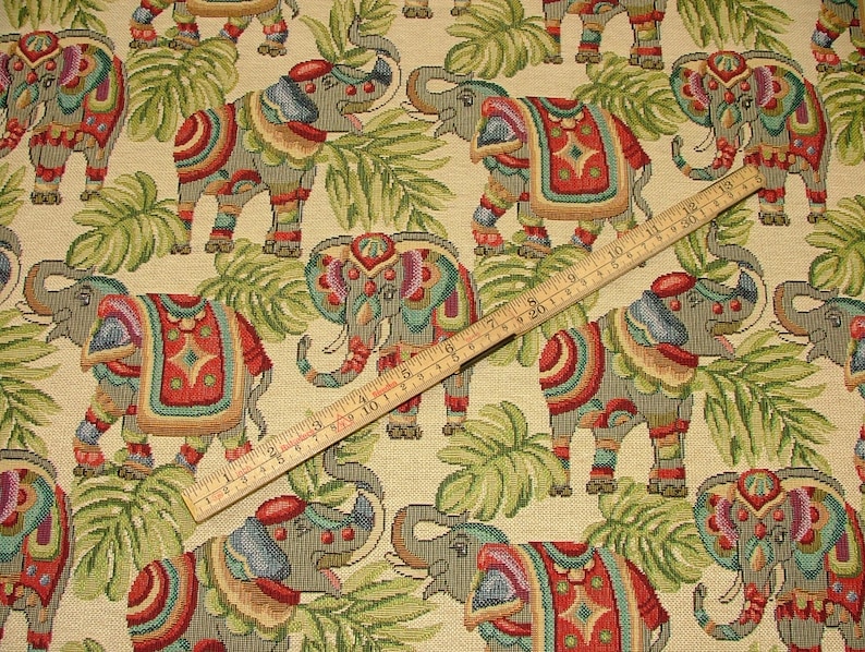 May include: Beige fabric with a repeating pattern of colorful elephants with intricate designs. The elephants are surrounded by green leaves.