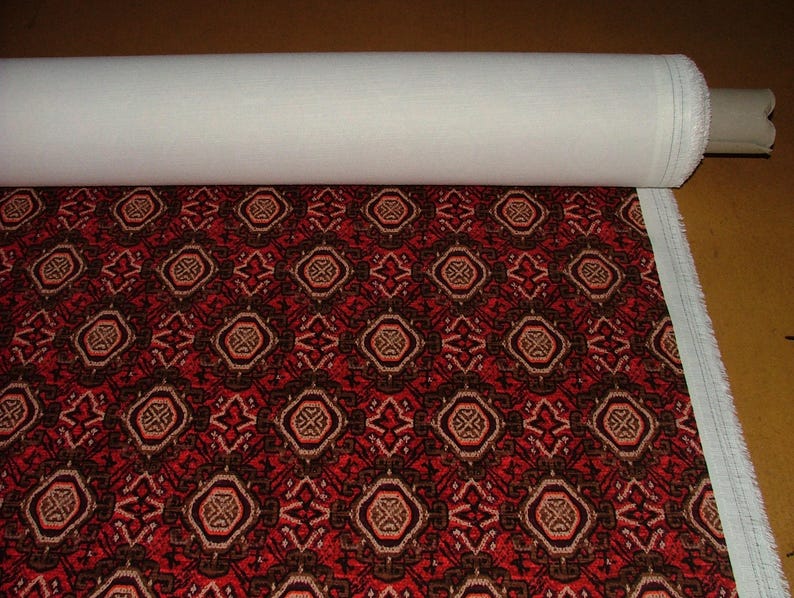 May include: A roll of fabric with a repeating geometric pattern in red, brown, and tan. The pattern features octagonal shapes with intricate designs. The fabric is partially unrolled, revealing a white backing.