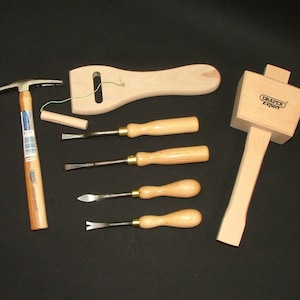 Puede incluir: Un conjunto de herramientas para trabajar la madera que incluye un martillo, un mazo y cuatro cinceles. Las herramientas están hechas de madera y metal y tienen un acabado natural.