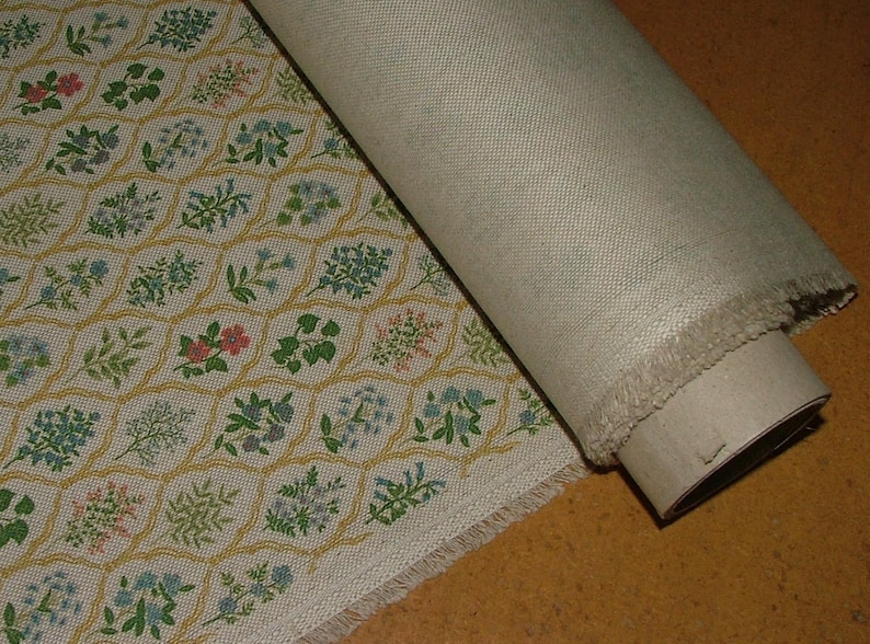 May include: A roll of beige fabric with a floral pattern. The pattern features small flowers in pink, blue, and green, set within a yellow honeycomb design. The fabric is partially unrolled, revealing the plain beige backing.