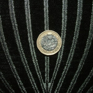 May include: A silver British one pound coin with a design of a thistle flower and the words "One Pound" on a black background with silver stripes.