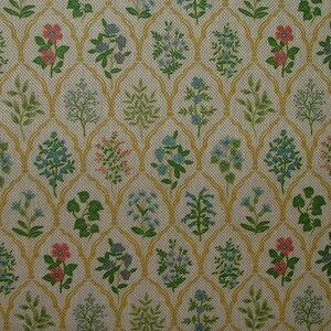 May include: A close-up of a fabric with a repeating floral pattern. The design features small flowers in shades of pink, blue, and green, set against a cream-coloured background. A gold-coloured trellis-like pattern frames the floral elements.