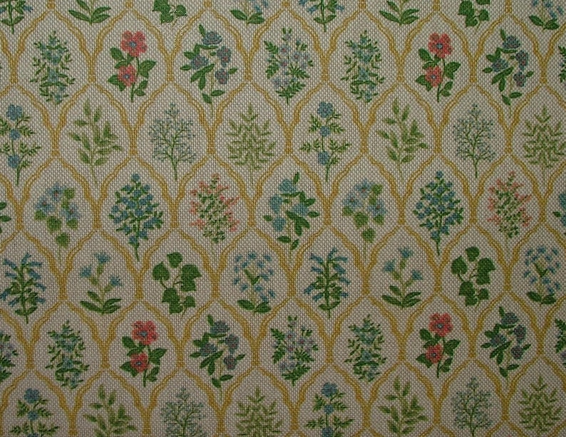 May include: A close-up of a fabric with a repeating floral pattern. The design features small flowers in shades of pink, blue, and green, set against a cream-coloured background. A gold-coloured trellis-like pattern frames the floral elements.