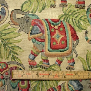 May include: A tapestry fabric featuring a repeating pattern of elephants with colorful decorations and green foliage. The fabric is beige with a woven texture.
