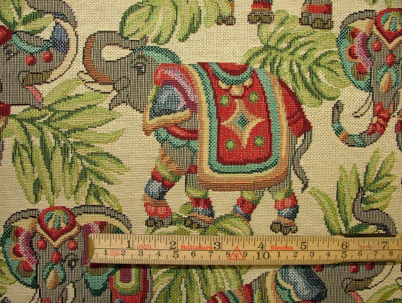 May include: A tapestry fabric featuring a repeating pattern of elephants with colorful decorations and green foliage. The fabric is beige with a woven texture.